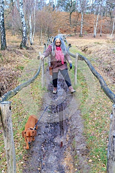 Senior woman with her dog trying to walk on muddy ground of trail with fence