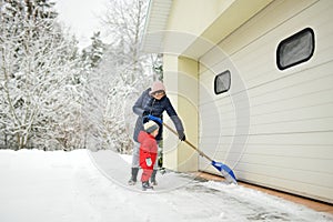 Senior woman and her little grandson shoveling snow off a walkway after massive snowfall. Small child helping outdoors