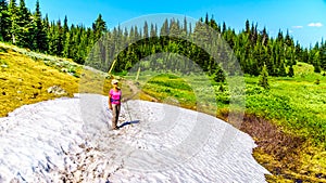 Senior woman hiking through a patch of snow surrounded by meadows with wildflowers