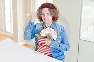 Senior woman holding beautiul bouquet of pink flowers annoyed and frustrated shouting with anger, crazy and yelling with raised