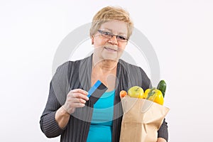 Senior woman holding fruits and vegetables in shopping bag and credit card, paying for shopping