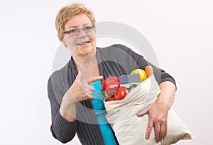 Senior woman holding fruits and vegetables in shopping bag and credit card, paying for shopping