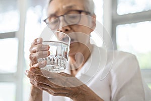 Senior woman holding glass of water,hand shaking while drinking water,elderly patient with hands tremor uncontrolled body tremors,