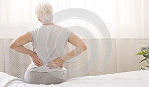 Senior woman holding her painful back in bed