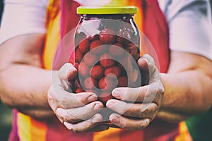 Senior woman holding a jar of cherry compote.