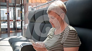 Senior woman holding modern smartphone in front of revolving doors