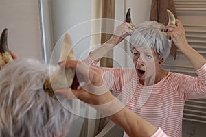 Senior woman holding pair of horns in front of the mirror