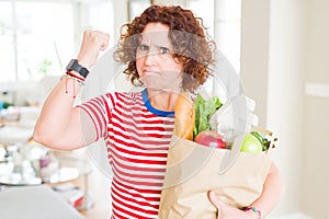 Senior woman holding paper bag full of fresh groceries from the supermarket annoyed and frustrated shouting with anger, crazy and