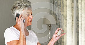 Senior woman holding pill bottle and talking on mobile phone in bedroom
