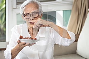 Senior woman holding plate of bad spoiled or expired food in her hand,rotten food,emitting a fetid smell or strong-smelling food, photo