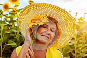 Senior woman holding sunflower in summer field enjoying nature. Happy woman relaxing outdoors