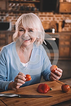 Senior woman holding tomatoes while cooking at kitchen
