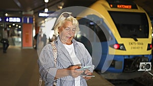 Senior woman holds biometric passport and train ticket waiting train on station platform. Railroad transport concept