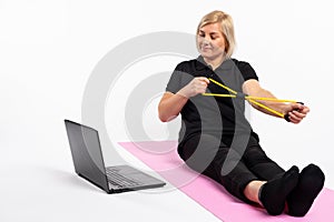 Senior woman holds a resistance band in front of laptop. Fitness online concept