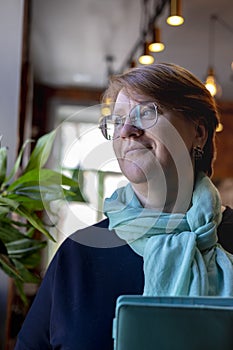 Senior woman holds stack of notebooks her hands while sitting by the window in small cafe