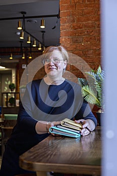 Senior woman holds stack of notebooks her hands while sitting by the window in small cafe