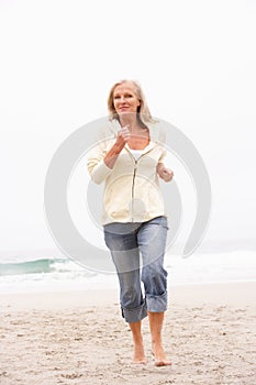 Senior Woman On Holiday Running Along Beach