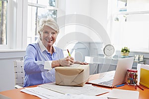 Senior Woman At Home Addressing Package For Mailing photo
