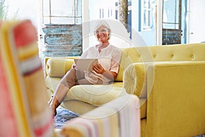 Senior Woman At Home In Lounge Using Digital Tablet