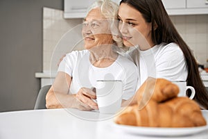 Senior woman hugging with granddaughter in kitchen.