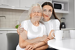 Senior woman hugging with granddaughter in kitchen.