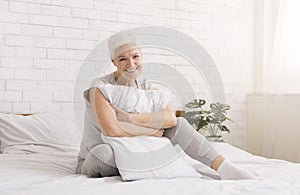 Senior woman hugging white pillow at home