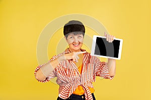 Senior woman isolated on yellow background. Tech and joyful elderly lifestyle concept