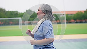 Senior woman jogging in outdoor stadium. Elderly female person is happy about cardio for health and wellness while walking or