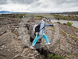 Senior woman is jumping over an earth gap at Thingvellir National Park -Iceland