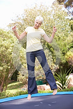 Senior Woman Jumping On Trampoline In Garden