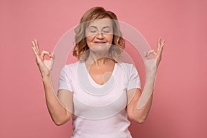 Senior woman keeping eyes closed while meditating, being calm and peaceful holding hands in mudra