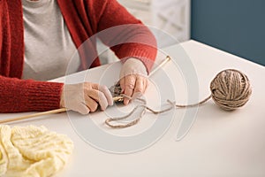 Senior woman knitting warm scarf at table