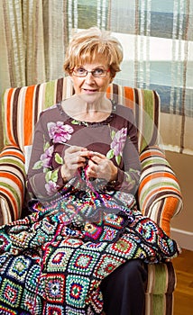 Senior woman knitting a wool quilt with patches