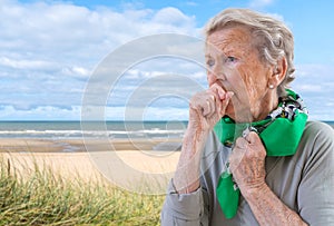 Senior woman l has bad cough, uses tissue, wears scarf on neck, feels unwell and unhealthy seaside background