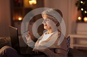 Senior woman with laptop and credit card at night