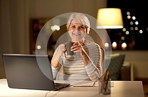 Senior woman with laptop drinking coffee at home