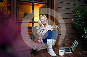 Senior woman with laptop and smartphone outdoors on terrace, working.