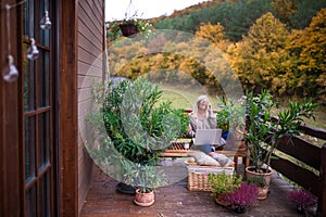 Senior woman with laptop and smartphone sitting outdoors on terrace.