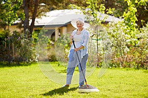 Senior woman with lawn rake working at garden