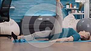 Senior woman lifting legs to do physical exercise on yoga mat