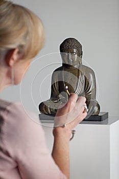 Senior woman lightens incense in front of a buddha statue