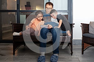 Senior woman and little girl and boy relax on sofa in patio have fun using cellphone together.