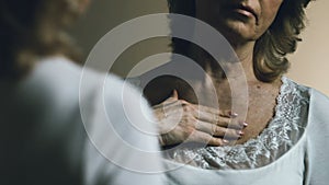 Senior woman looking at her reflection, upset with aging and sagging skin