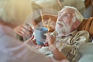Senior woman looking at her sick spouse and and offering tea