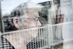 Senior woman looking out through a window like depress photo