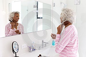 Senior Woman Looking At Reflection In Bathroom Mirror Brushing Hair