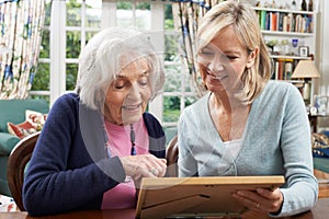 Senior Woman Looks At Photo Frame With Mature Female Neighbor