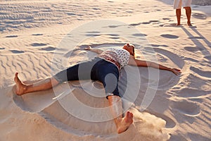 Senior Woman Lying On Beach Making Sand Angel On Vacation