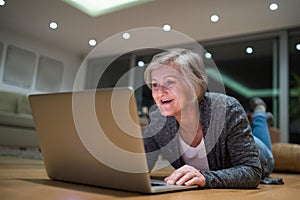 Senior woman lying on the floor working on laptop