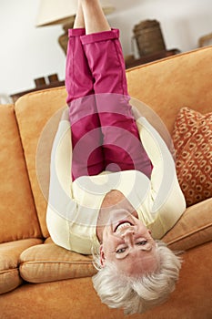 Senior Woman Lying Upside Down On Sofa At Home